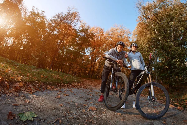 Felice giovane coppia che va a fare un giro in bicicletta in una giornata autunnale nel parco, retroilluminazione . — Foto Stock