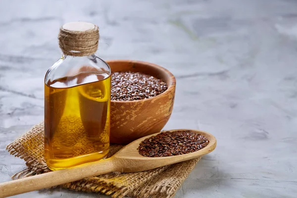 Flax seeds in bowl and flaxseed oil in glass bottle on light textured background, top view, close-up, selective focus