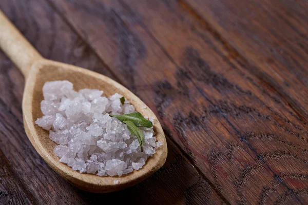 Crystal sea salt in a wooden spoon over vintage wooden background, top view, close-up, selective focus