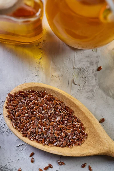 Semillas de lino en cuenco y aceite de linaza en botella de vidrio sobre fondo texturizado claro, vista superior, primer plano, enfoque selectivo — Foto de Stock