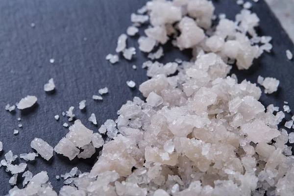 Pile of salt crystals over the dark board on white background, close-up, top view, macro, selective focus