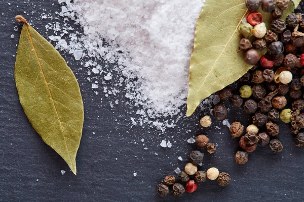 Composition of bay laurel leaf with peppercorn and salt isolated on dark background, top view, close-up, selective focus