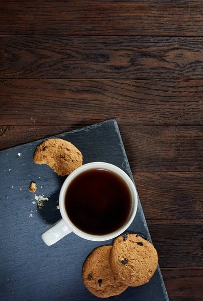 Taza de té con un par de galletas en pizarra negra sobre un fondo de madera, vista superior, enfoque selectivo — Foto de Stock