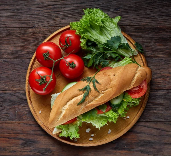 Panino fresco con lattuga, pomodori e formaggio servito su un piatto di legno su fondo di legno, attenzione selettiva — Foto Stock