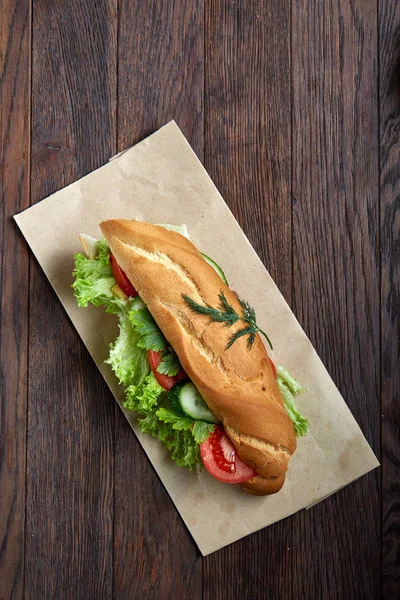 Panino fresco e gustoso con formaggio e verdure su un piatto di carta su sfondo di legno, messa a fuoco selettiva, vista dall'alto — Foto Stock