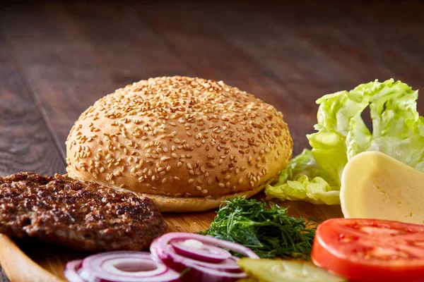 Yummy hamburger ingredients artistically organized on wooden plate, close-up, top view, selective focus