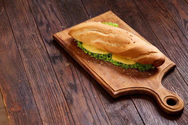 Fresh and tasty sandwich with cheese and vegetables on cutting board over wooden background, selective focus. — Stock Photo, Image