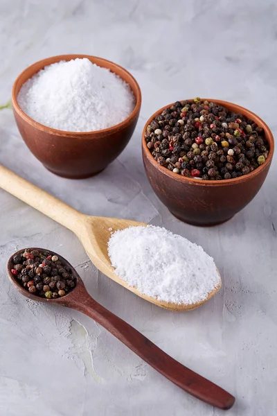 Conceptual composition of salt and pepper on spoons and bowls over light background, top view, close-up