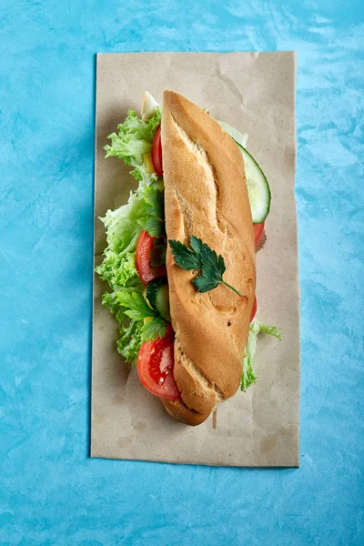 Färska och läckra smörgås med ost och grönsaker på papper plattan över Blå bakgrund, selektivt fokus, ovanifrån — Stockfoto
