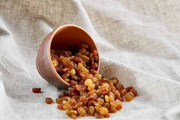 Overturned ceramic bowl with golden raisins on light tablecloth, close-up, selective focus