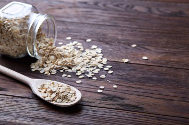 Devrilmiş cam kavanoz ve kaşık vintage ahşap arka plan, yakın çekim, seçici odak çiğ yulaf ezmesi ile.