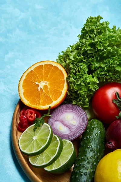 Still life of fresh organic vegetables on wooden plate over blue background, selective focus, close-up