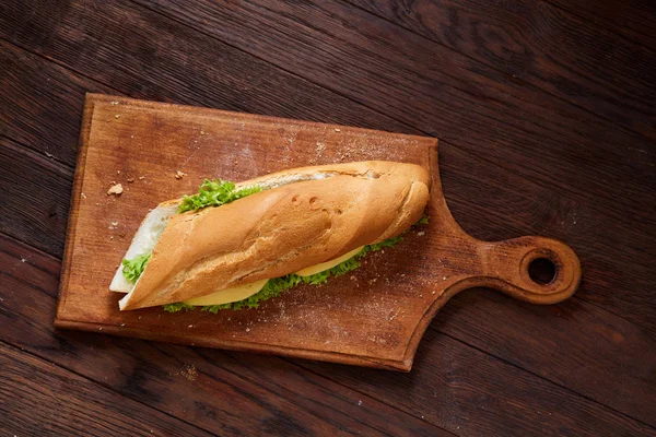 Fresh and tasty sandwich with cheese and vegetables on cutting board over wooden background, selective focus. — Stock Photo, Image