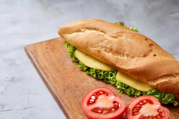 Fresh and tasty sandwich with cheese and vegetables on cutting board over white textured background, selective focus. — Stock Photo, Image