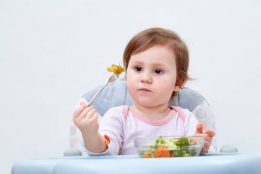 Çok güzel bebek kız beyaz zemin üzerine haşlanmış sebze yemek yerken eğleniyor