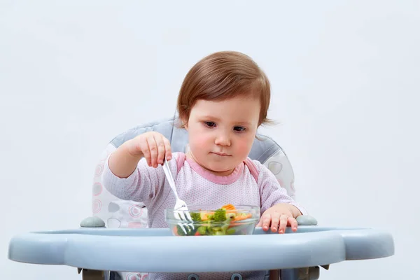 Menina da criança adorável está se divertindo enquanto come legumes cozidos no fundo branco — Fotografia de Stock
