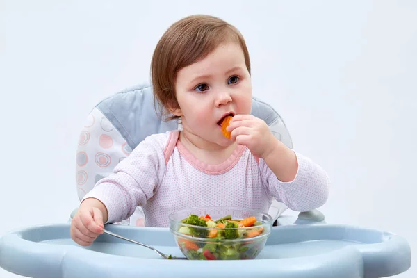 Menina da criança adorável está se divertindo enquanto come legumes cozidos no fundo branco — Fotografia de Stock