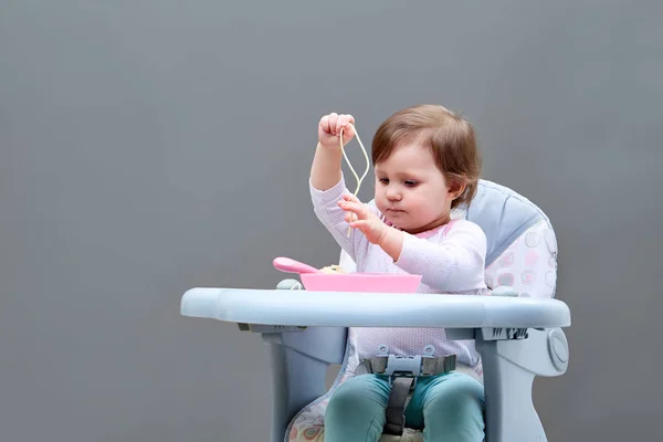 Adorable niña está divirtiéndose mientras come verduras guisadas sobre fondo gris — Foto de Stock