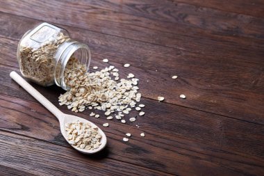 Devrilmiş cam kavanoz ve kaşık vintage ahşap arka plan, yakın çekim, seçici odak çiğ yulaf ezmesi ile.