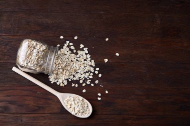 Devrilmiş cam kavanoz ve kaşık vintage ahşap arka plan, yakın çekim, seçici odak çiğ yulaf ezmesi ile.