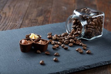 Ahşap zemin, seçici odak üzerine devrilmiş cam sürahi kahve çekirdekleri ve çikolata şekerleme ile yan görünüm