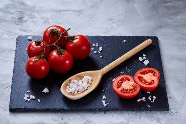 Taze domates ve bir kaşık tuz beyaz arka plan, yakın çekim, seçici odak Siyah Taşlı gemide.