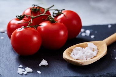 Taze domates ve bir kaşık tuz beyaz arka plan, yakın çekim, seçici odak Siyah Taşlı gemide.