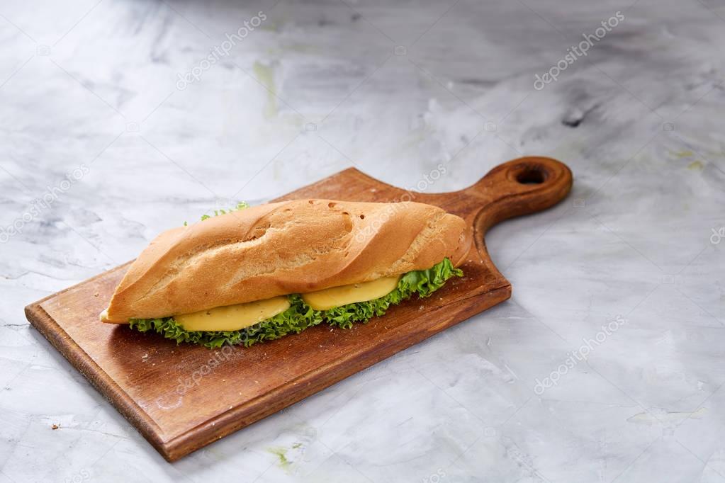 Fresh and tasty sandwich with cheese and vegetables on cutting board over white textured background, selective focus.