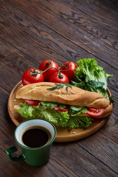 Fresh sandwich with lettuce, tomatoes, cheese on wooden plate, cup of coffee on wooden background, selective focus — Stock Photo, Image