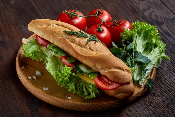 Panino fresco con lattuga, pomodori e formaggio servito su un piatto di legno su fondo di legno, attenzione selettiva — Foto Stock