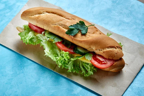 Fresh and tasty sandwich with cheese and vegetables on paper plate over blue background, selective focus, top view — Stock Photo, Image