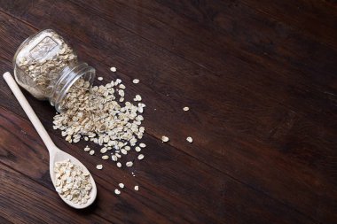 Devrilmiş cam kavanoz ve kaşık vintage ahşap arka plan, yakın çekim, seçici odak çiğ yulaf ezmesi ile.