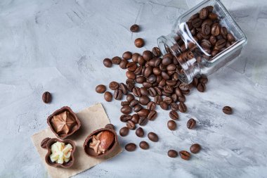 Beyaz arka planda, seçici odak devrilmiş cam sürahi kahve çekirdekleri ve çikolata şekerleme ile yan görünüm