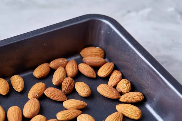 Raw almond on baking tray over white textured background, selective focus, shallow depth of field.