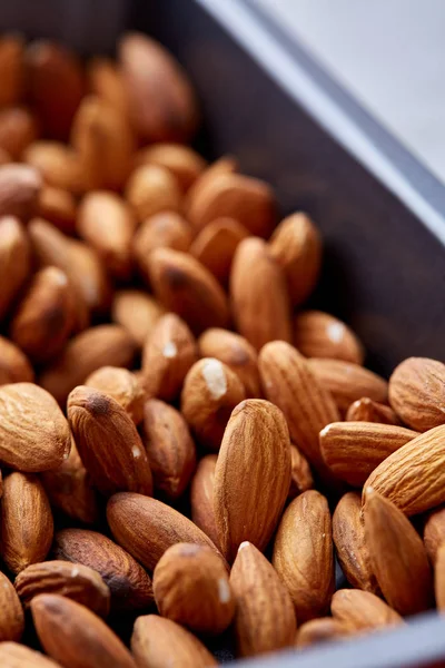 Raw almond on baking tray over white textured background, selective focus, shallow depth of field.