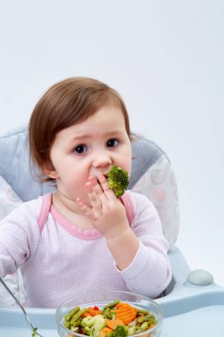 Çok güzel bebek kız beyaz zemin üzerine haşlanmış sebze yemek yerken eğleniyor