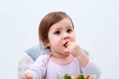 Çok güzel bebek kız beyaz zemin üzerine haşlanmış sebze yemek yerken eğleniyor
