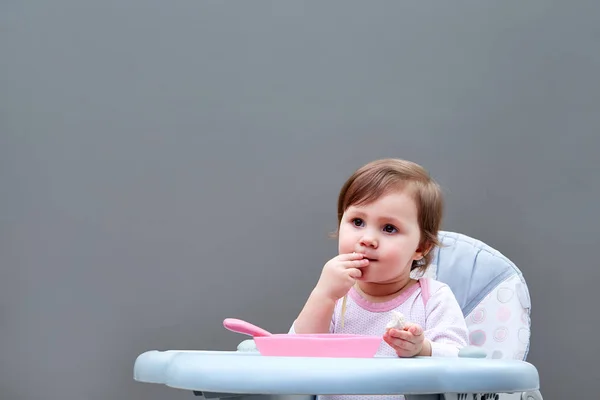 Menina da criança adorável está se divertindo enquanto come legumes cozidos no fundo cinza — Fotografia de Stock