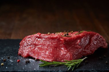 Çiğ et dana biftek siyah üzerine kurulu baharat ve biberiye ile ahşap arka plan üzerinde seçici odak kayrak