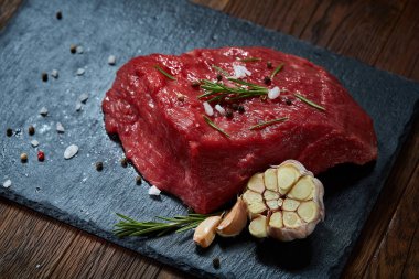 Çiğ et dana biftek siyah üzerine kurulu baharat, sarımsak ve biberiye ile ahşap arka plan üzerinde seçici odak kayrak