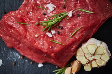 Çiğ et dana biftek siyah üzerine kurulu baharat, sarımsak ve biberiye ile ahşap arka plan üzerinde seçici odak kayrak