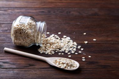 Devrilmiş cam kavanoz ve kaşık vintage ahşap arka plan, yakın çekim, seçici odak çiğ yulaf ezmesi ile.