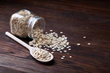 Devrilmiş cam kavanoz ve kaşık vintage ahşap arka plan, yakın çekim, seçici odak çiğ yulaf ezmesi ile.