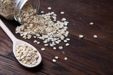 Devrilmiş cam kavanoz ve kaşık vintage ahşap arka plan, yakın çekim, seçici odak çiğ yulaf ezmesi ile.