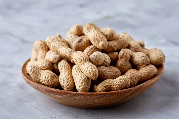 Unpeeled peanuts in wooden bowl over rustic wooden background closeup, selective focus