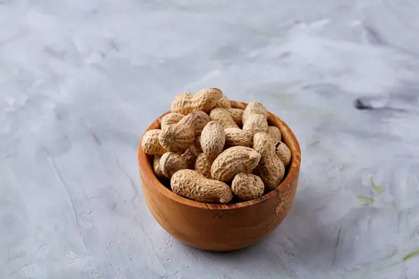 Unpeeled peanuts in wooden bowl over rustic wooden background closeup, selective focus