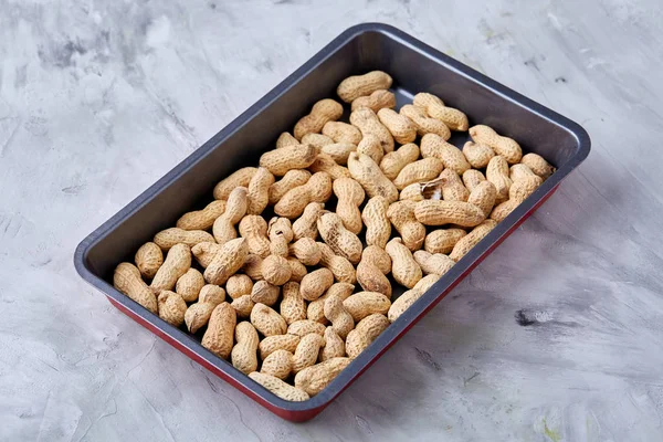 Unpeeled raw peanut on baking tray over white textured background, selective focus, shallow depth of field.