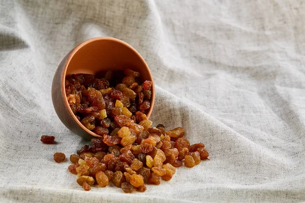 Overturned ceramic bowl with golden raisins on light tablecloth, close-up, selective focus — Stock Photo, Image
