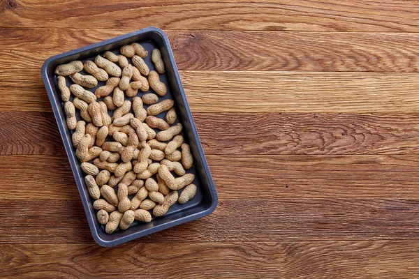 Unpeeled raw peanut on baking tray over wooden background, selective focus, shallow depth of field.