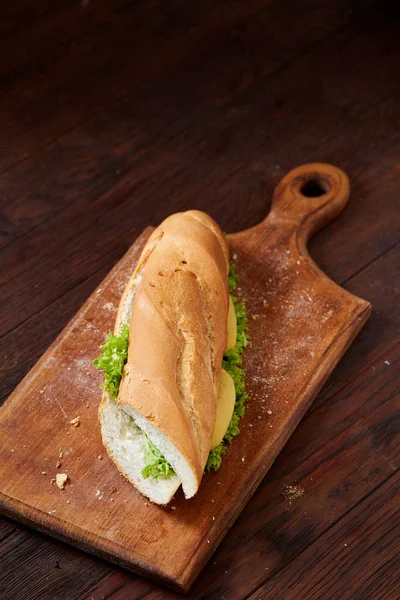 Fresh and tasty sandwich with cheese and vegetables on cutting board over wooden background, selective focus.